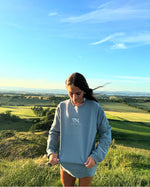 Gracie Elloy stands in Edinburgh, Scotland, United Kingdom, wearing neverthirst's 'Proclaim Good News' sweatshirt featuring a minimalist line graphic of a world map on a sage green sweatshirt.